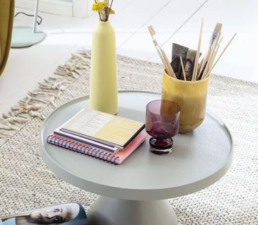 Runder niedriger Beistelltisch in grau dekoriert mit einem Block, Vase und einem Behälter mit Pinseln.