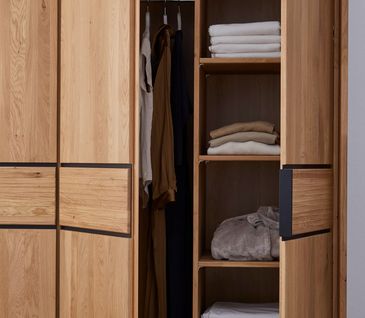 Innenansicht eines Massivholzschrankes mit Kleiderstange und Regalen mit Kleidung gefüllt.