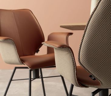 Zwei Lederstühle gegenüber voneinander, die außen mit Stoff bezogen sind und innen mit Leder in Kupfer.