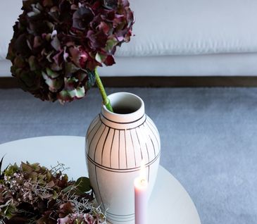 Vase mit dunkelroter Hortensie neben Blumenkranz und rosa Kerze