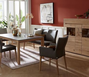 Graue Lederstühle um Holzesstisch mit schwarzer Tischplatte neben Sideboard aus Massivholz.