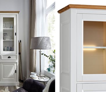 Weiße Vitrine Im Landhausstil mit Glastüren und Einlegeböden unterhalb Schubladen und Schiebetüren.