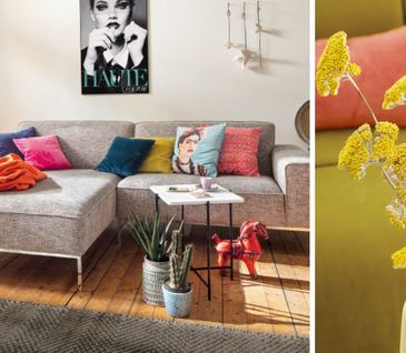 Bunte Kissen und Decken auf grauem Ecksofa neben einer gelben Vase mit gelben Blumen