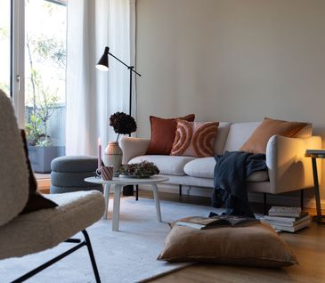 Weißes Sofa mit herbstlichen Kissen, Hocker in Grau und Sessel mit Flausch