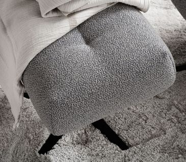 Grauer Design-Hocker auf dem eine Decke liegt.