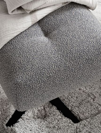 Grauer Design-Hocker auf dem eine Decke liegt.