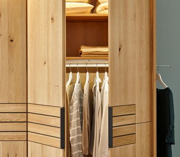 Halb geöffneter Kleiderschrank aus Massivholz mit schwarzen Akzenten.