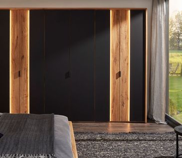 Schwarzer Drehtürenschrank mit Akzenten in Massivholz und Beleuchtung an den Türen