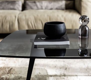 Moderner Couchtisch aus Metall mit Tischplatte aus Rauchglas mit dunkler Deko.