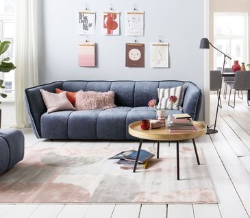 Blaues 3-Sitzer Sofa mit bunten Deko-Kissen vor einer Wand mit Bildern.