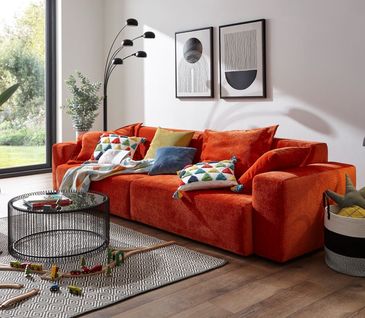 Oranges Sofa mit bunten Kissen dekoriert vor einer Wand mit Bildern.
