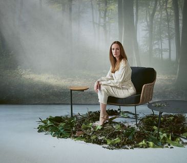 Frau sitzt auf Outdoor-Sessel zwischen zwei Beistelltischen.