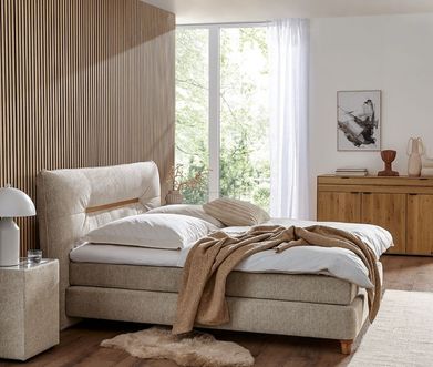 Beiges Boxspringbett mit Matratze und Topper mit heller Bettwäsche.