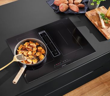 Gemüse in einer Pfanne auf einem Induktionskochfeld in dunkler Küche