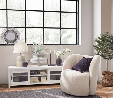 Wohnzimmer im modernen Landhausstil mit weißem Sessel und Lowboard mit Pflanzen dekoriert.