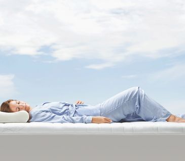 Frau schläft in hellblauem Pyjama auf Matratze ohne Bettlaken.