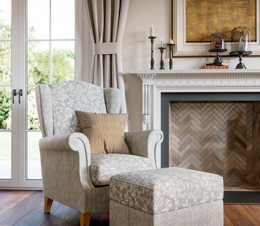 Ohrensessel in Beige mit passendem Hocker vor Kamin.