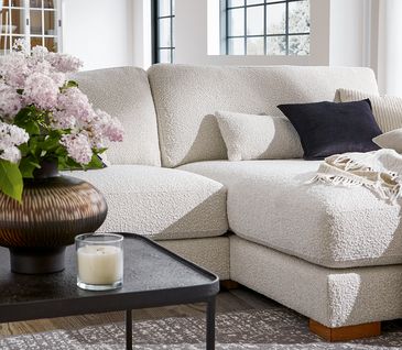 Bauchige Vase mit Blumen auf einem Couchtisch vor beigem Sofa.