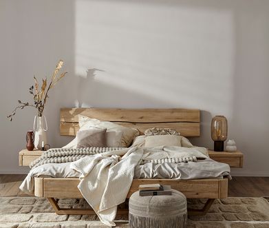 Holzbett in hellem Schlafzimmer mit beigen Kissen und beiger Decke mit Beistelltischen auf beiden Seiten in Holz.