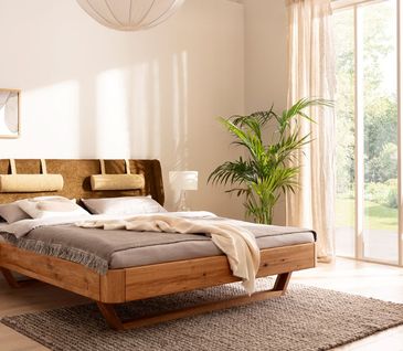 Massives Bettgestell mit moosgrünem Kopfteil vor weißer Wand