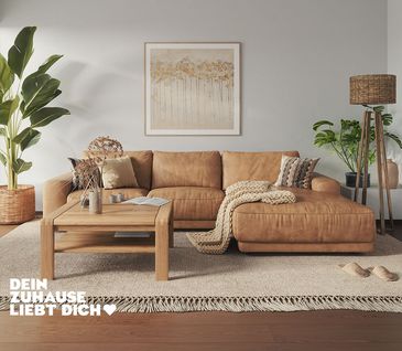 Ecksofa mit hellbraunem Lederbezug in hellem Wohnzimmer mit beigem Teppich und Couchtisch aus Holz.