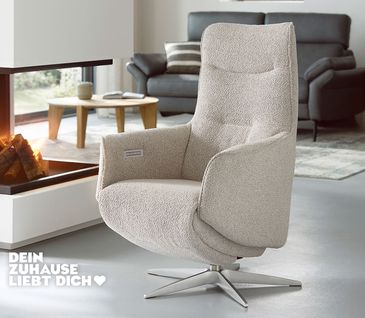 Relaxsessel mit hellgrauem Stoffbezug und silbernem Sterngestell vor modernem Kamin.