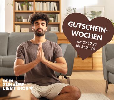 Junger Mann sitzt im Schneidersitz in natürlich eingerichtetem Wohnzimmer und entspannt sich.