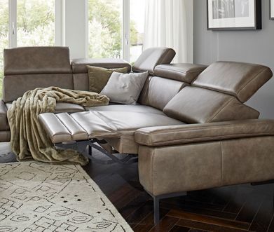 Graubraunes 3-Sitzer Sofa aus Leder mit einer Relaxfunktion und grünem und grauem Deko-Kissen.
