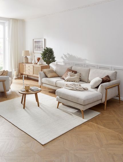 Wohnzimmer im Landhaus-Stil mit beigem Ecksofa, passendem Sessel und Sideboard aus hellem Holz.