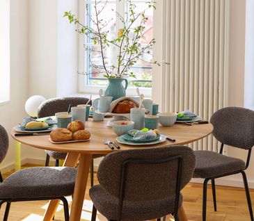 Esszimmertisch mit vier grauen Stühlen: eingedeckt und dekoriert für ein Frühlings-Frühstück.