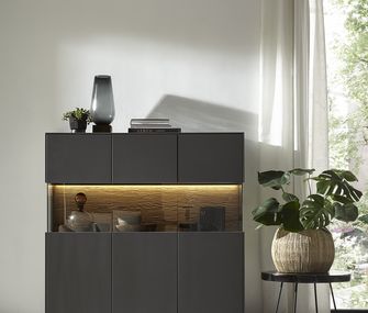 Sideboard dekoriert mit Deko-Vase, Deko-Flasche und anderen Deko-Objekten neben Beistelltisch mit Pflanze in Jute-Übertopf.