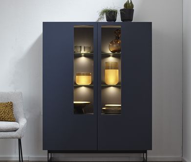 Blaues Highboard mit Vitrinenscheiben vor weisser Wand.