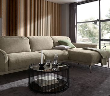 Ecksofa in gedecktem Grün in modernem, hellen Wohnzimmer mit grauem Teppich und Wandpaneelen aus Holz.