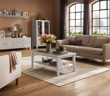 Helles Wohnzimmer im Landhausstil mit beigem Sofa, passendem Sessel, weißem Cochtisch  und weißem Sidebaord.