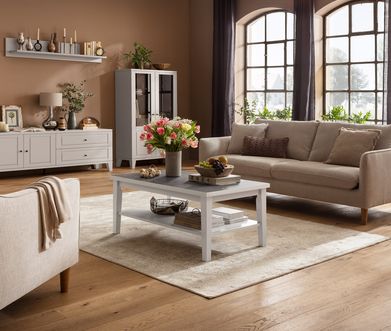 Helles Wohnzimmer im Landhausstil mit beigem Sofa, passendem Sessel, weißem Cochtisch  und weißem Sidebaord.