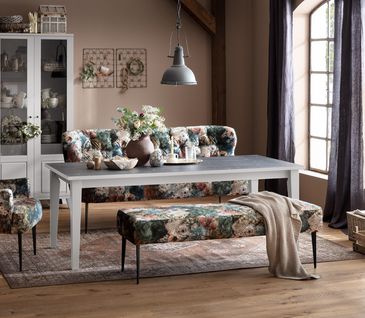 Esszimmer im Landhaus-Stil mit Bänken und Stuhl in floralem Design, großem Esstisch und weißer Vitrine.