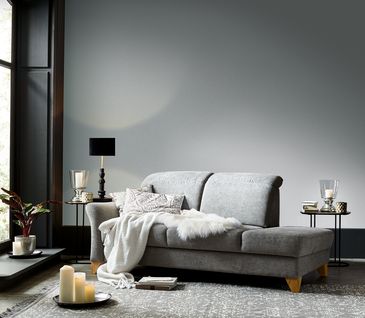 Hellgraue Liege fürs Wohnzimmer dekoriert mit Kissen und Decken.