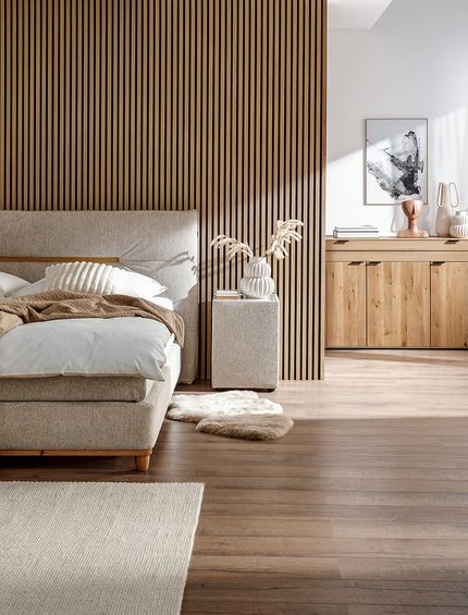 Weißes Boxspringbett neben Massivholzmöbeln im hellen Schlafzimmer.