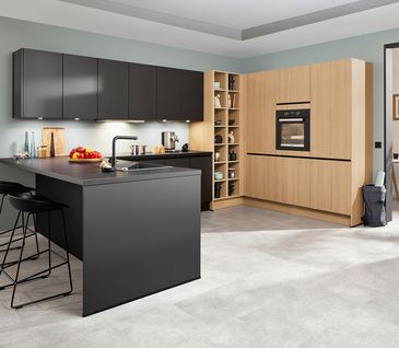 Offene Wohnküche mit Tresen in Schwarz und Küchenelementen aus Holz.