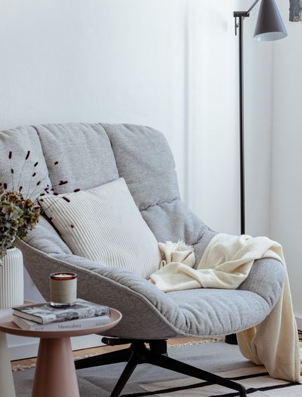 Hellgrauer Sessel mit schwarzem Metallgestell, dekoriert mit Kissen und Decke in Beige.