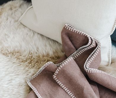 Detailansicht von brauner Decke, weißem Kissen und beigem Kunstfell.