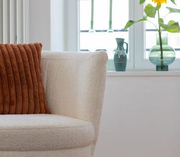 Beiges Bouclé-Sofas, dekoriert mit rotbraunem Kissen neben einem Fenster dekoriert mit Vasen und Sonnenblume.