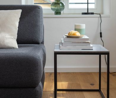 Minimalistischer Beistelltisch mit Metallgestell und Keramikplatte in einem Wohnzimmer.