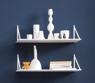 Weißes Wandregal mit weißer Dekoration vor einer dunkelblauen Wand