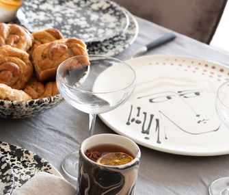 Gesicht auf Geschirr neben Gläsern und Bechern mit schwarz-weißem Muster