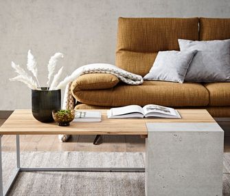Beton und Holz vereinen Kühle und Wärme auf eine besonders stilvolle Weise Couchtisch aus Massivholz und Beton vor goldenem Sofa