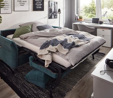 Blaues Sofa umgebaut in ein bequemes Bett mit grauer Bettwäsche