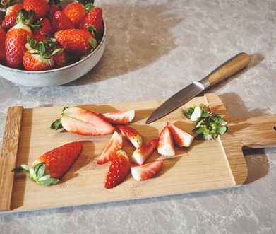 Schneidebrett mit Messer und geschnittenen Erdbeeren auf Marmorarbeitsplatte