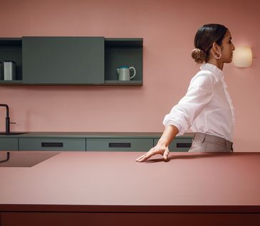 Frau in einer roten Küche mit oliv-farbigen Details und Hand auf Arbeitsfläche