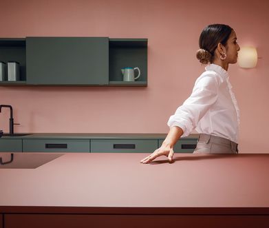 Frau in einer roten Küche mit oliv-farbigen Details und Hand auf Arbeitsfläche